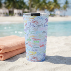 Blue Autographs tumbler beside a peach towel on a tropical beach