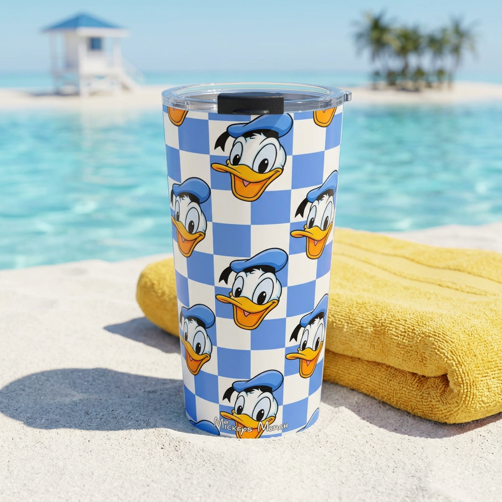 Donald tumbler beside a yellow towel on a tropical beach