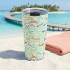 Green Autographs tumbler beside a coral towel overlooking a tropical lagoon