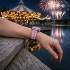 Pink bow-pattern watchband beside a glowing waterfront carousel