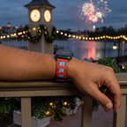 Red winter-scene watchband beside an illuminated waterfront clock tower